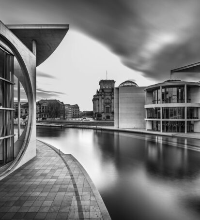 Grayscale shot of a lake in the middle of city buildings under a cloudy sky