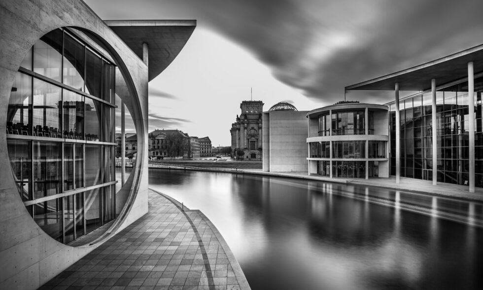 Grayscale shot of a lake in the middle of city buildings under a cloudy sky