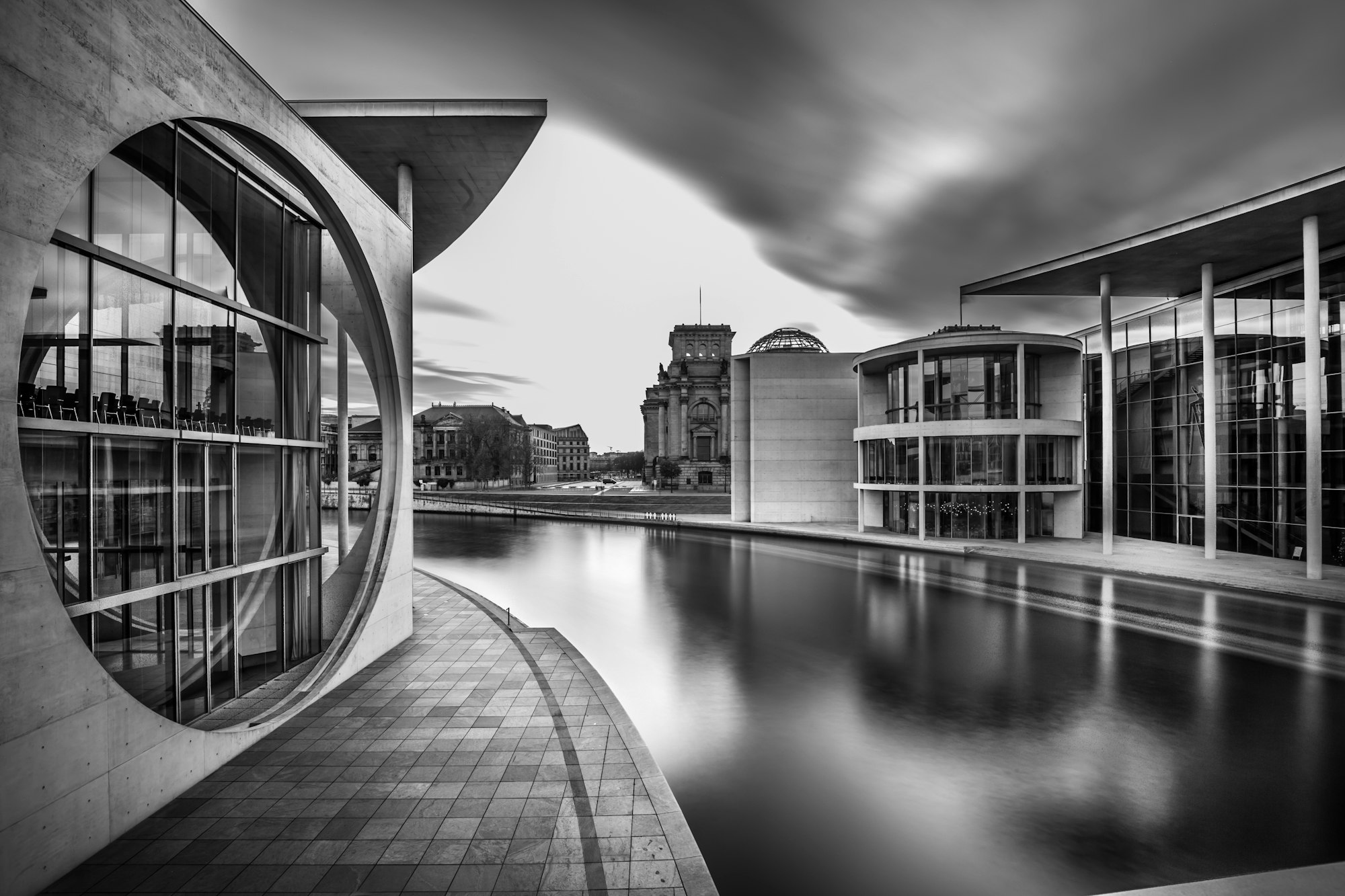 Grayscale shot of a lake in the middle of city buildings under a cloudy sky